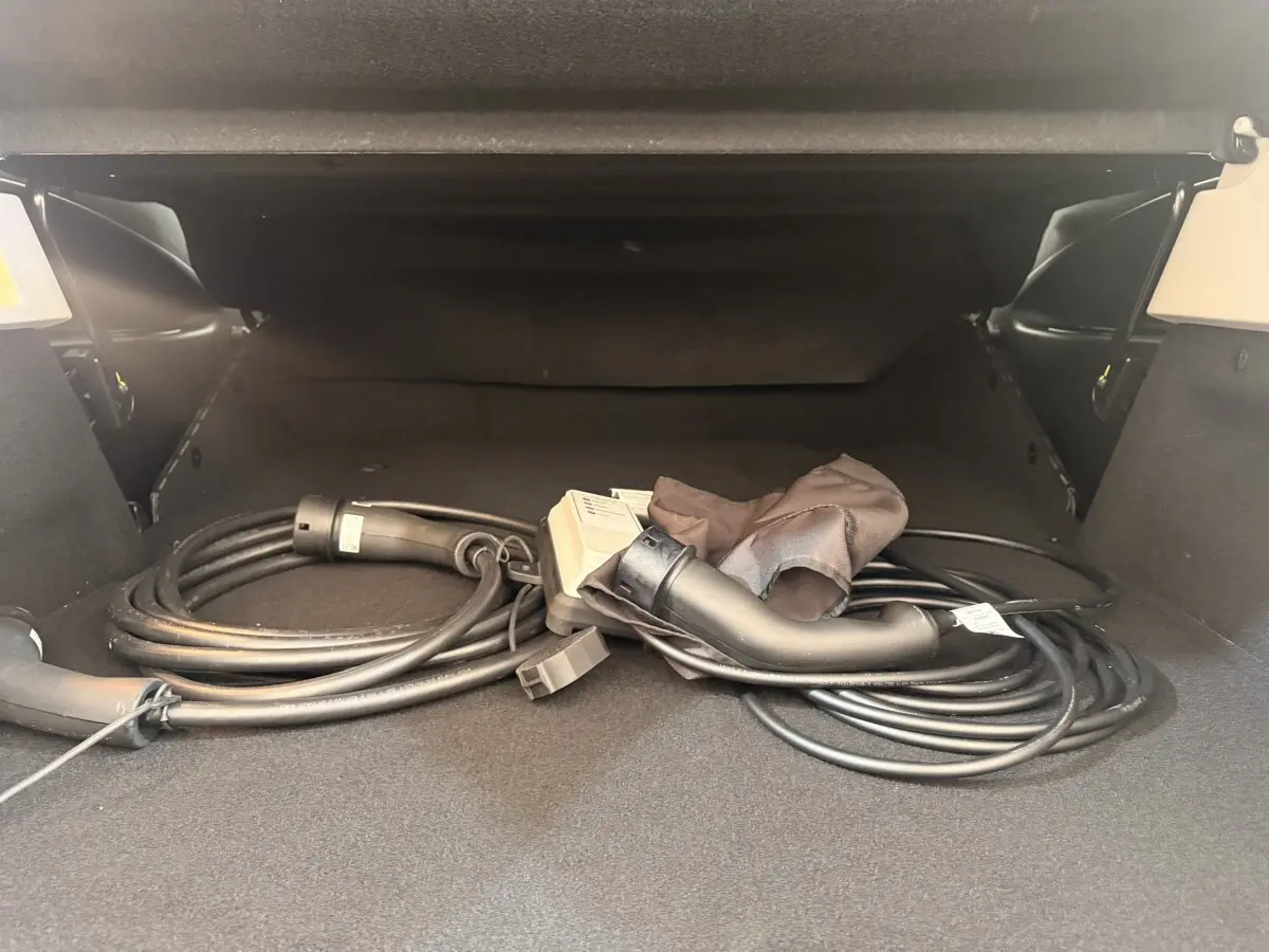 Coffre ouvert d'une Renault ZOE noire avec câble de charge électrique enroulé visible au centre.