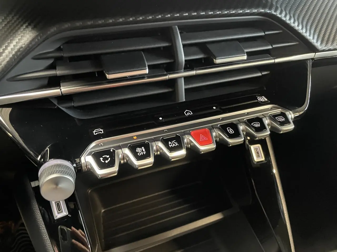 Vue rapprochée de la console centrale noire brillante du Peugeot 2008 bleu, avec commandes tactiles et boutons chromés.