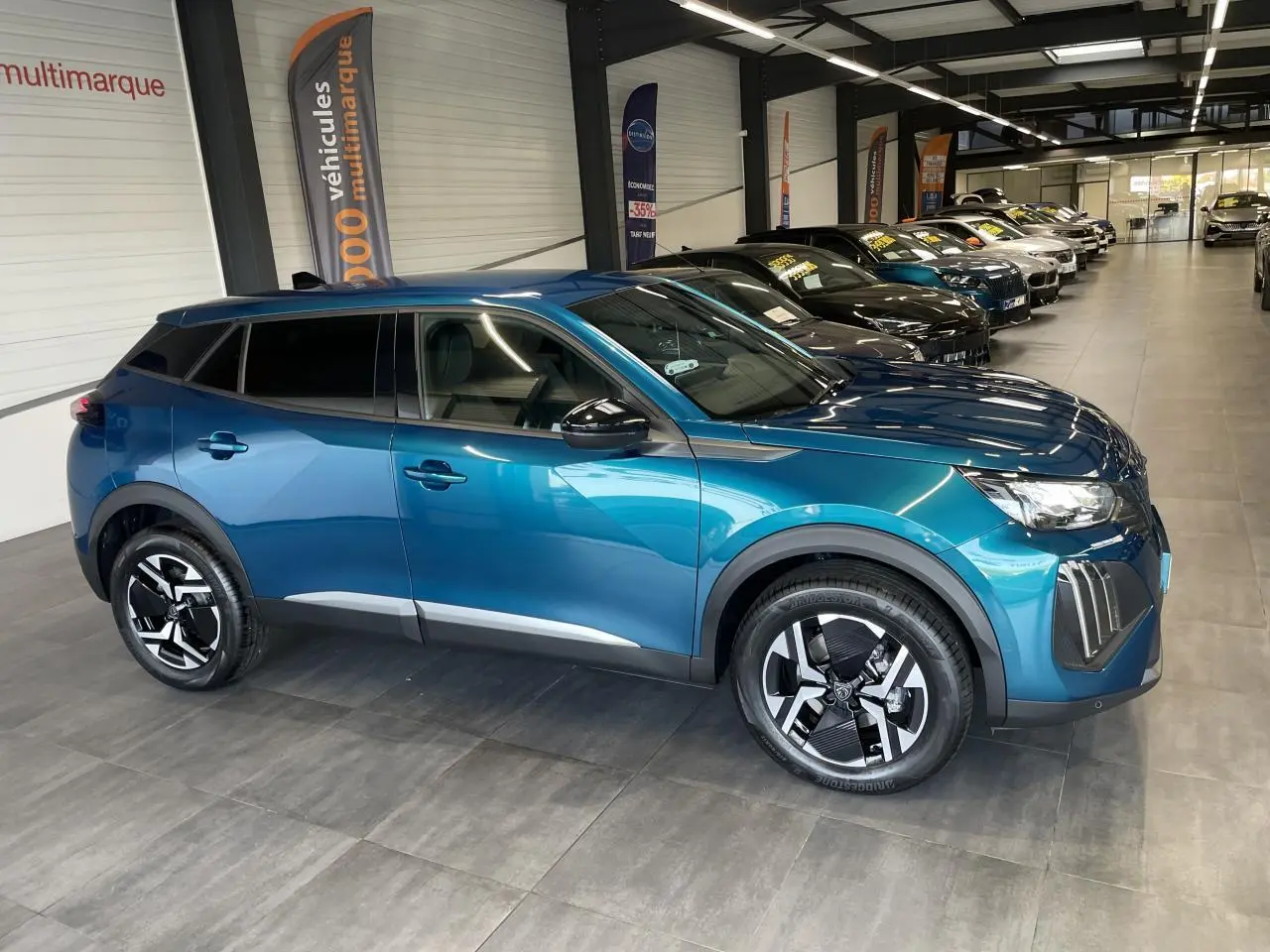 Peugeot 2008 bleu 3/4 avant droit en showroom, jantes alliage bicolores et vitres teintées.