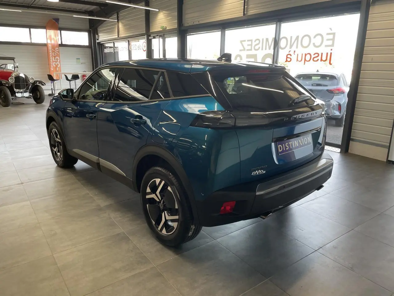Peugeot 2008 bleu 3/4 arrière droit en intérieur, jantes alliage bicolores et feux arrière LED 3 griffes visibles.