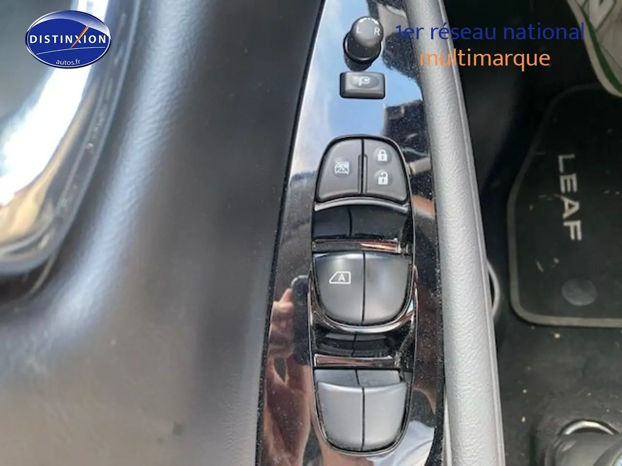 Gros plan sur les commandes de lève-vitres côté conducteur d'une Nissan Leaf blanche nacrée 2019, tapis avec logo Leaf visible.