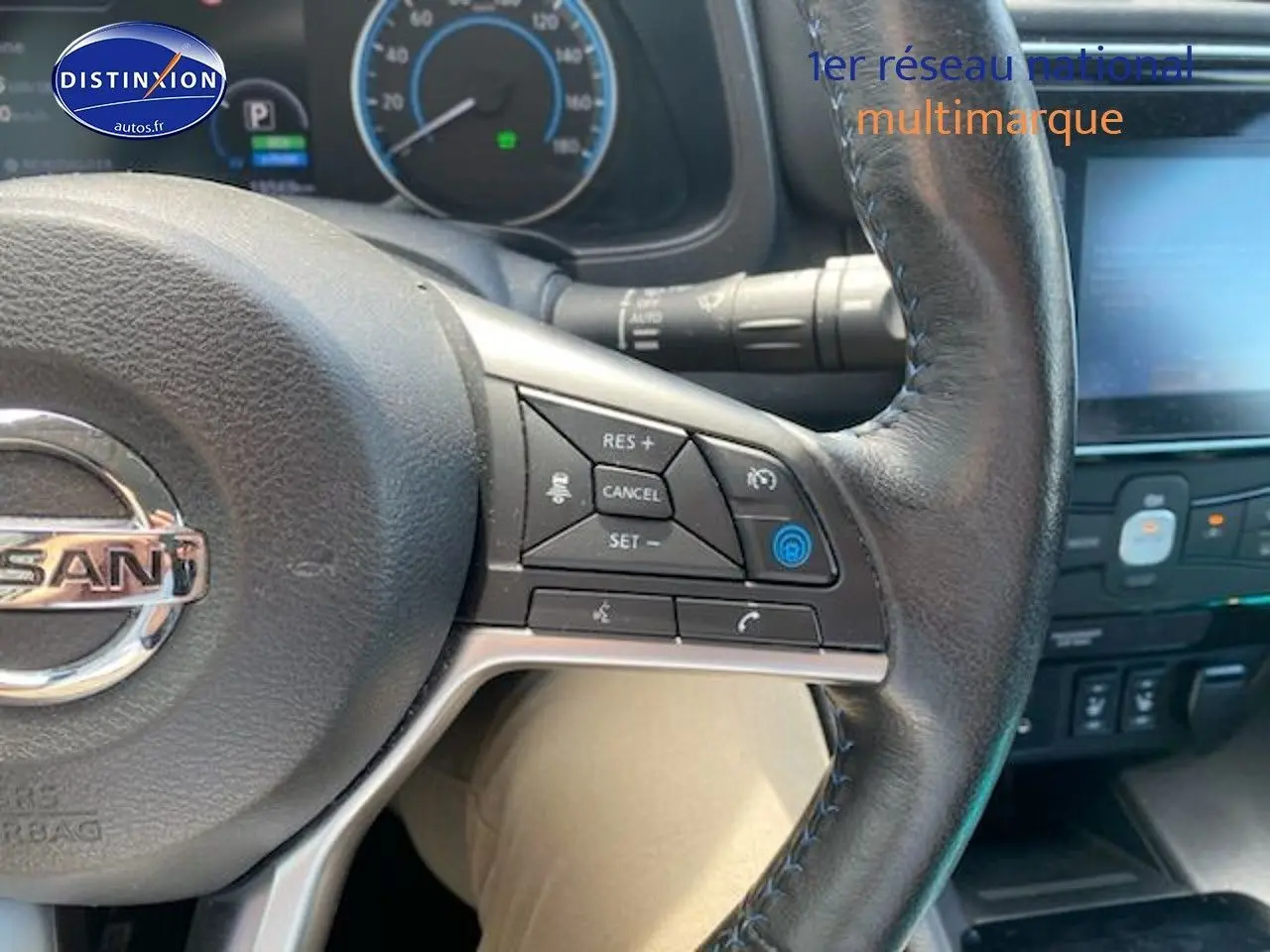 Vue rapprochée du volant en cuir noir de la Nissan Leaf électrique blanche nacrée, avec commandes intégrées visibles.