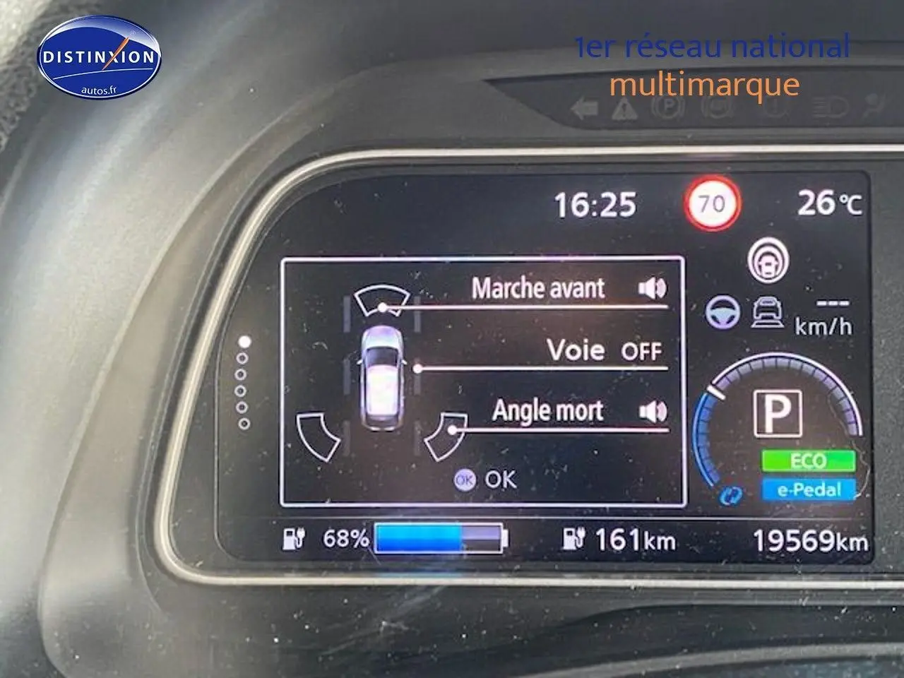 Tableau de bord numérique de Nissan Leaf blanche nacrée, affichant l'état de conduite et l'autonomie à 68% batterie.