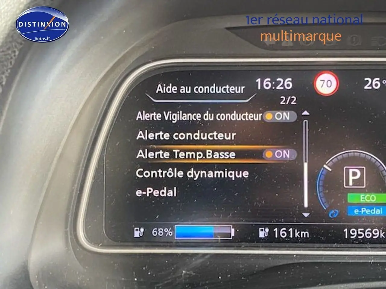Tableau de bord numérique de Nissan Leaf blanche nacrée, affichant alertes et autonomie à 68% de charge.