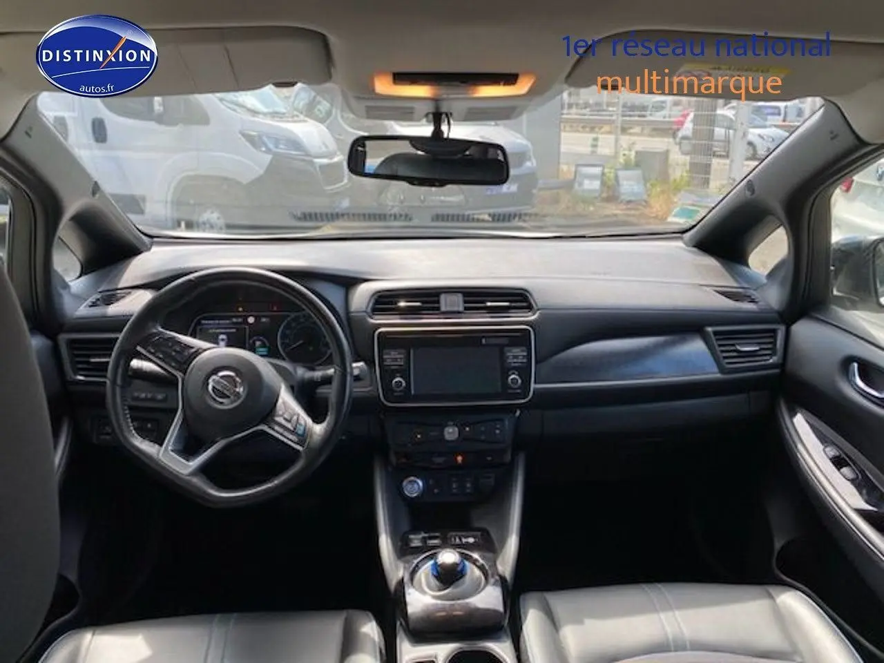 Vue intérieure du tableau de bord et volant du Nissan Leaf blanc nacré, avec écran tactile central et commandes modernes.