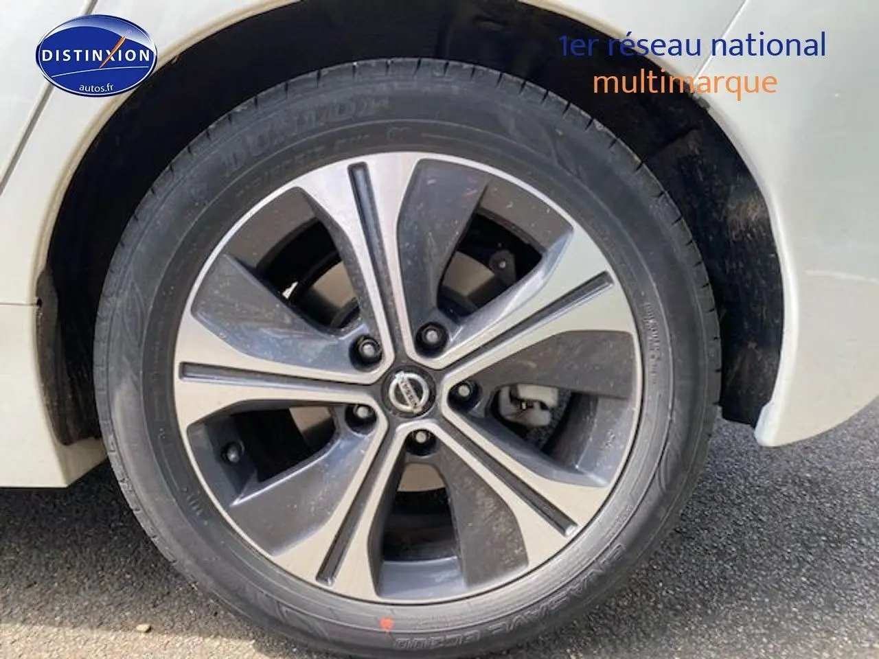 Gros plan sur la roue avant gauche d'une Nissan Leaf électrique 2019 blanc nacré avec jante alliage bicolore.