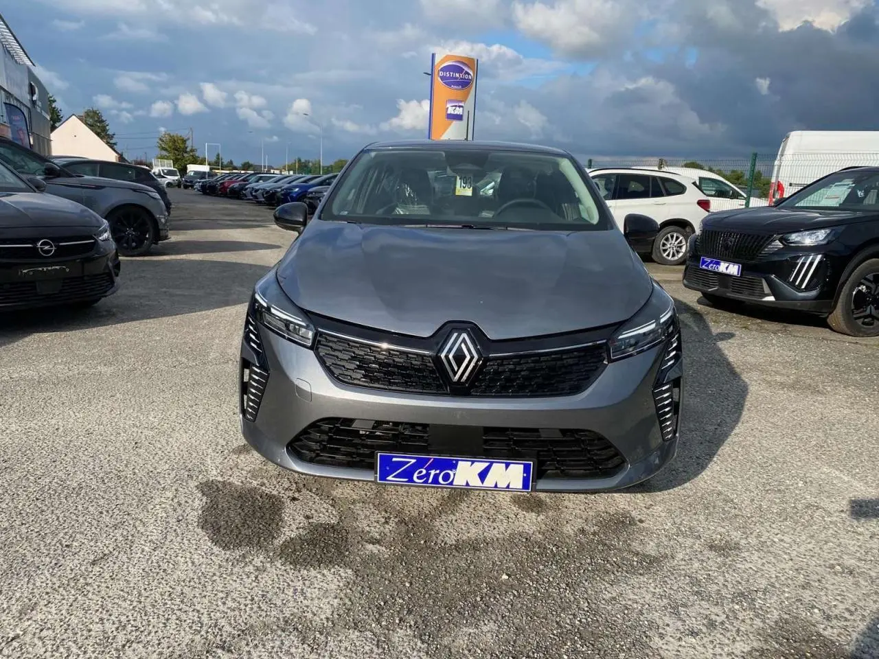 Renault Clio gris schiste vue de face sur parking, avec calandre noire et phares LED distinctifs allumés.