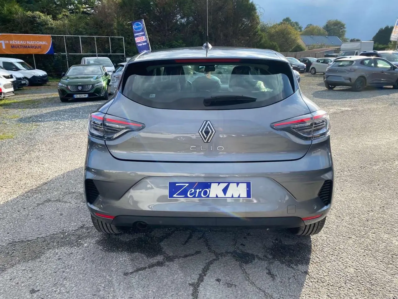 Vue arrière d'une Renault Clio 2025 gris schiste avec feux LED et plaque Zéro KM sur un parking extérieur.