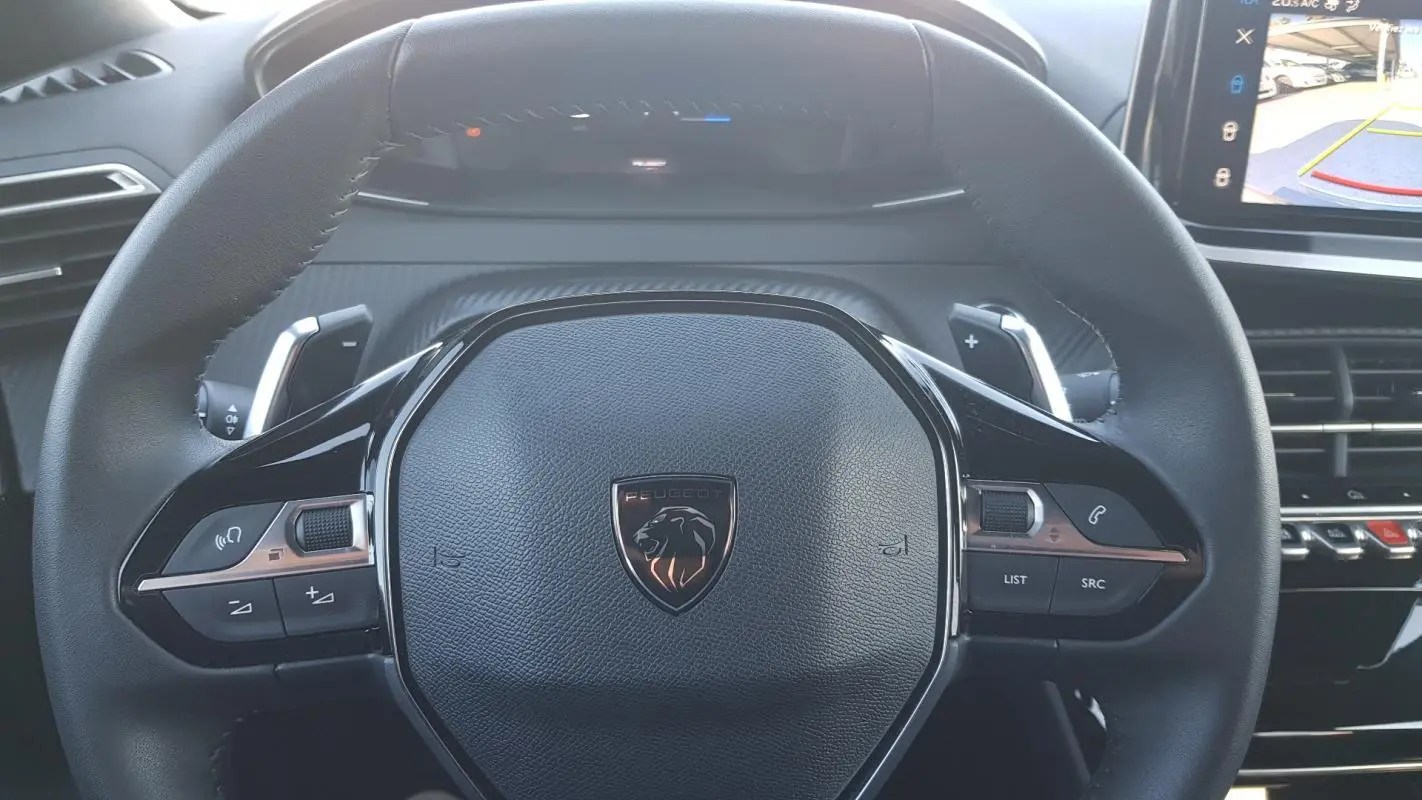 Gros plan sur le volant noir du Peugeot 2008 Hybrid 145 Allure avec commandes intégrées et logo lion central.