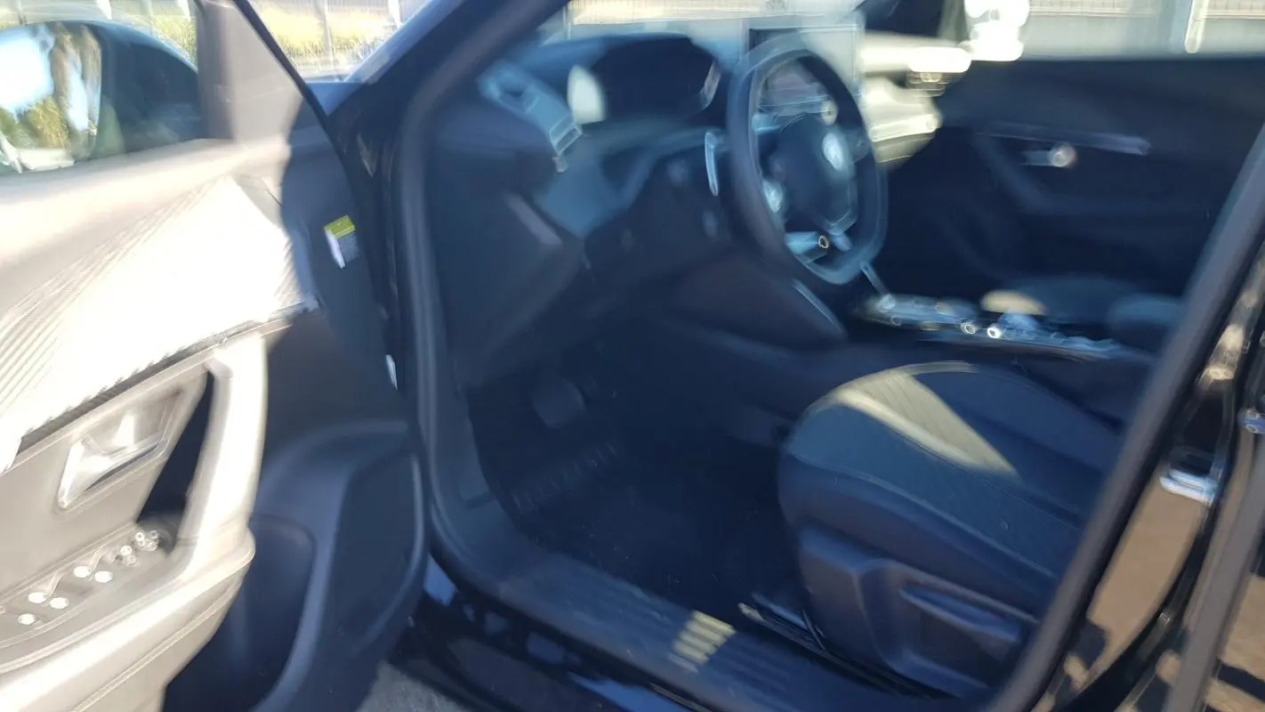 Intérieur avant gauche d’un Peugeot 2008 Hybrid 145 noir, montrant siège conducteur et tableau de bord flou.
