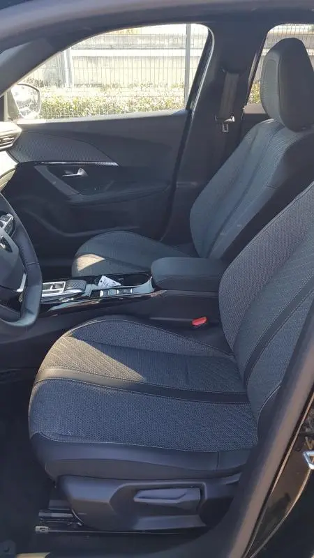 Vue intérieure côté conducteur du Peugeot 2008 Hybrid 145 Allure 2025 noir, sièges tissu gris et console centrale moderne.