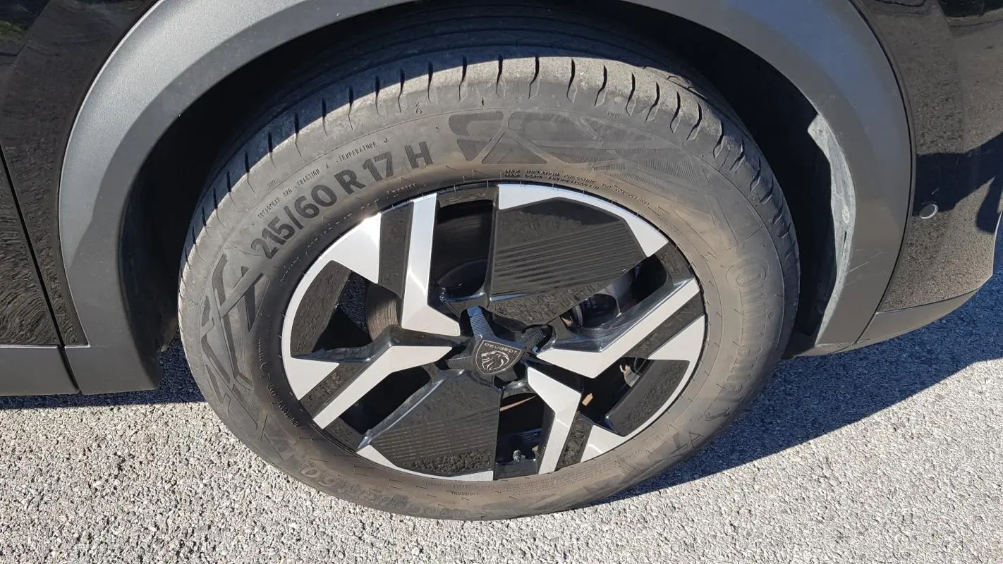 Gros plan sur la jante alliage 17 pouces noire et argentée du côté gauche d’un Peugeot 2008 Hybrid 145 Allure noir.