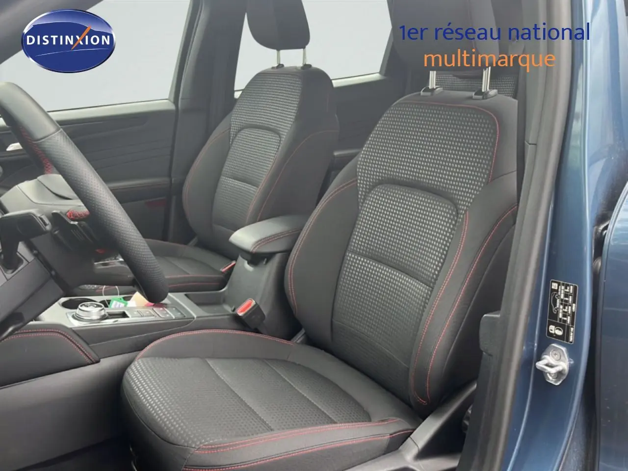 Vue intérieure côté conducteur du Ford Kuga bleu chrome métal 2024, sièges tissu noir avec surpiqûres rouges.