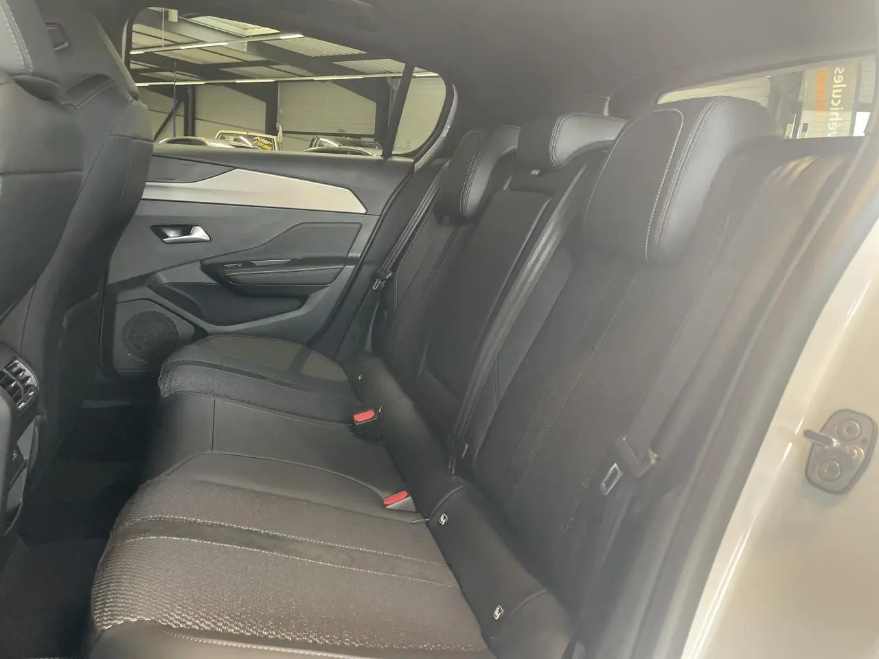 Vue intérieure côté droit sur la banquette arrière noire avec surpiqûres et porte blanc métallisé d'une Peugeot 308 GT 2025.