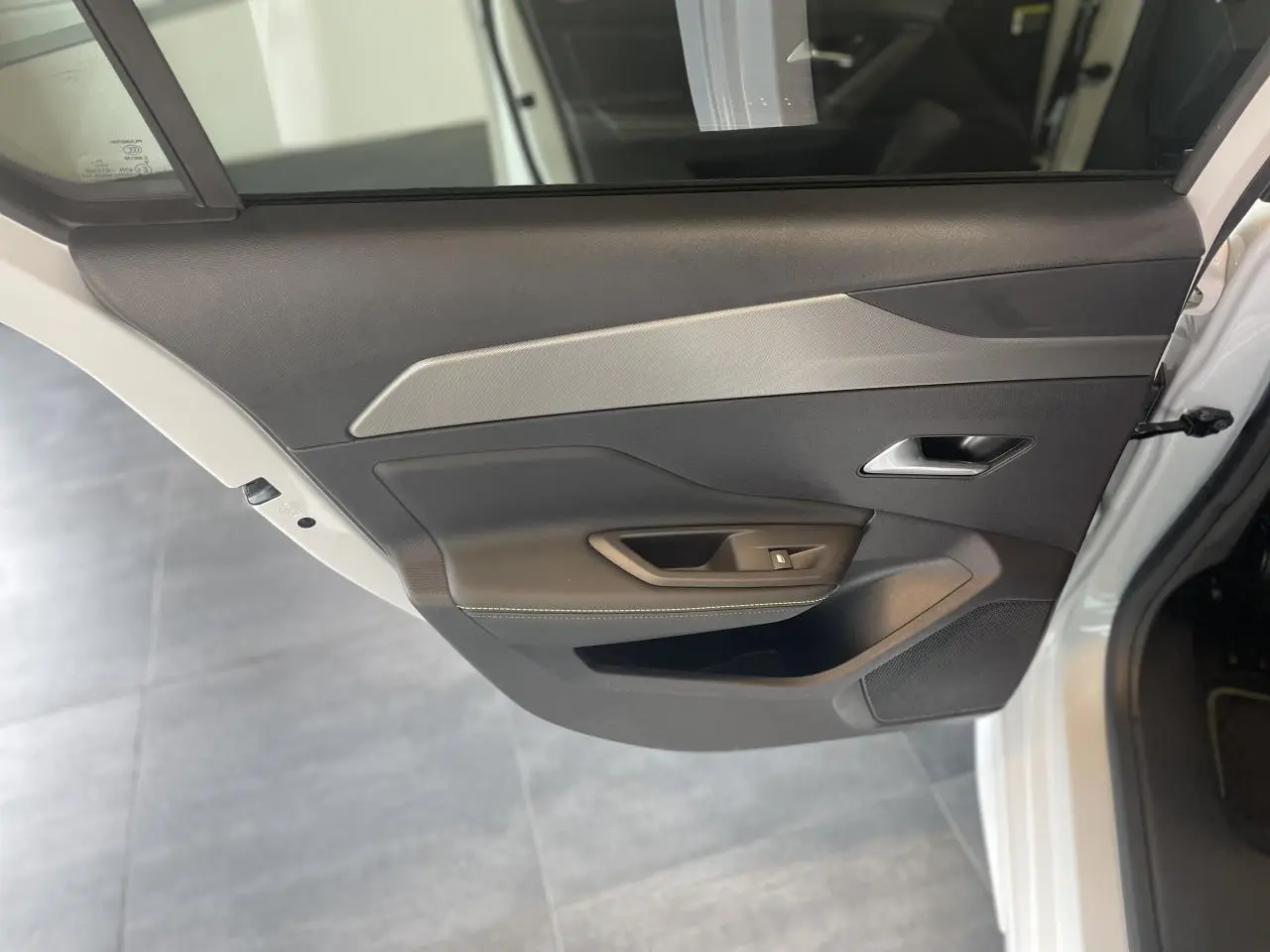 Porte arrière gauche ouverte d'une Peugeot 308 blanche, avec garniture noire et insert gris clair texturé.