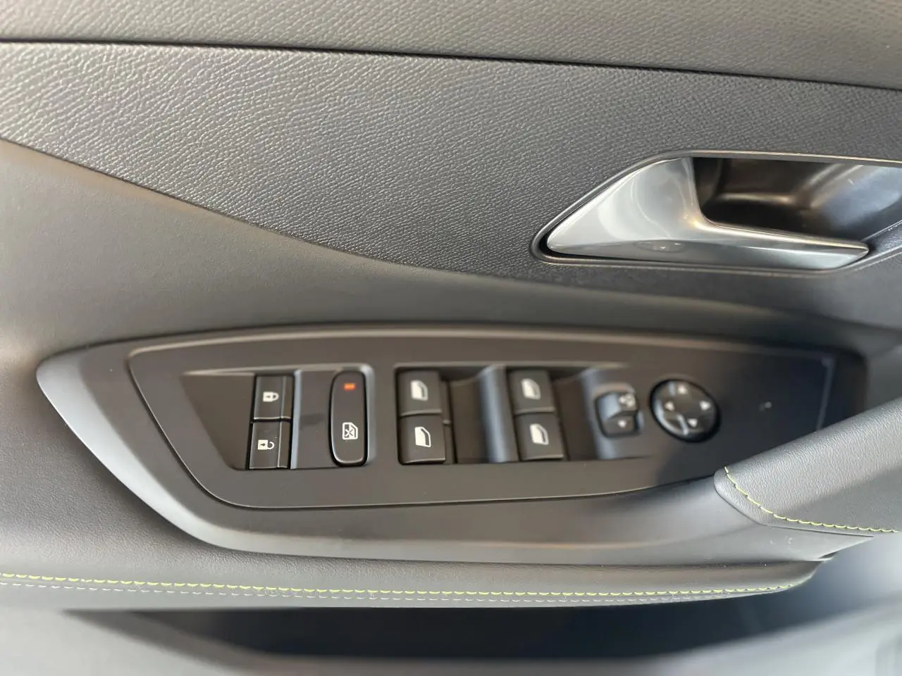 Gros plan sur la commande des vitres et rétroviseurs côté conducteur de la Peugeot 308 blanche, avec surpiqûres vertes.
