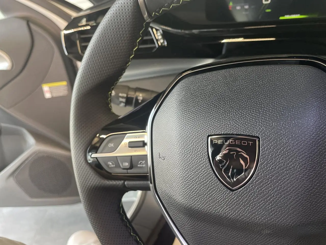 Gros plan sur le volant cuir noir de la Peugeot 308 2025 avec logo lion et commandes intégrées côté gauche.