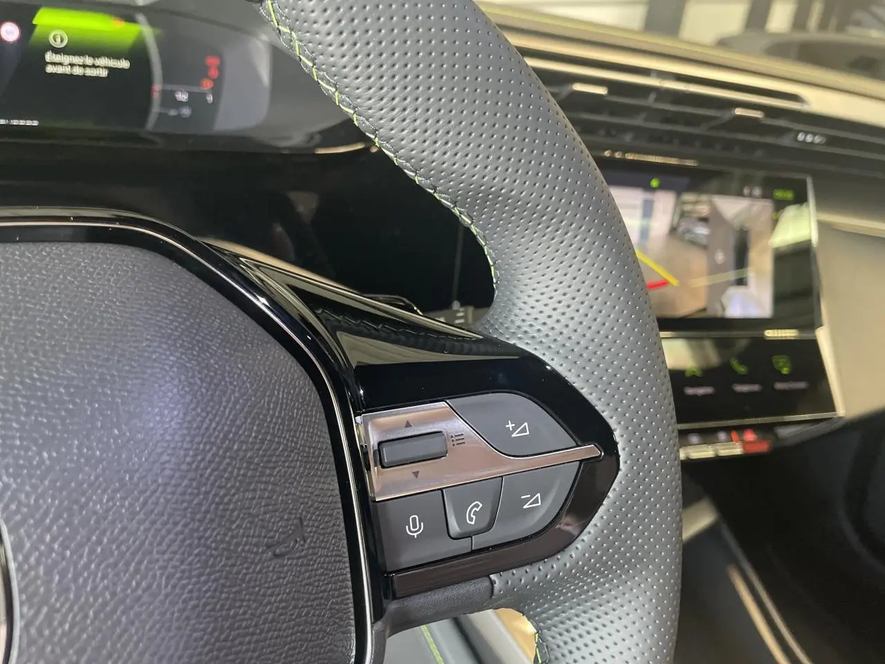 Gros plan sur le volant cuir perforé avec commandes intégrées et écran numérique du tableau de bord de la Peugeot 308 blanche.