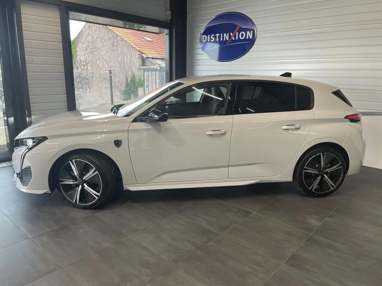 Peugeot 308 blanche vue de profil côté gauche en intérieur, avec jantes alliage noires et vitres teintées.
