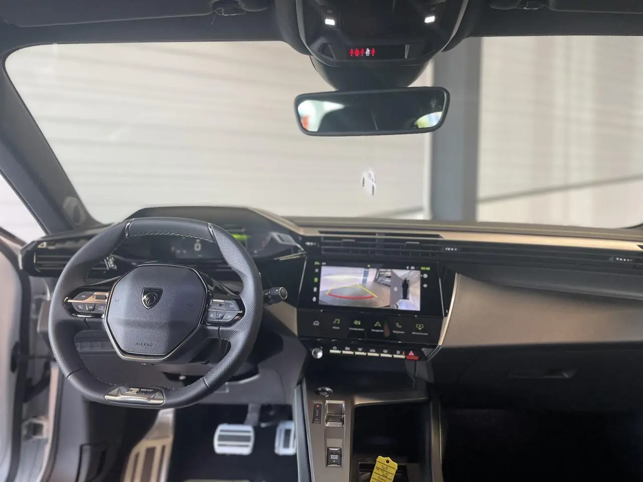 Vue intérieure avant de la Peugeot 308 blanche 2025, volant cuir, écran tactile avec caméra de recul affichée.