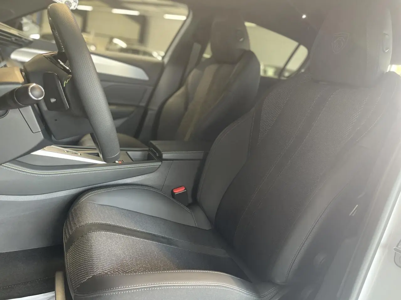 Intérieur de la Peugeot 308 GT 2025, vue côté conducteur sur sièges tissu/TEP noirs avec logo Peugeot brodé.