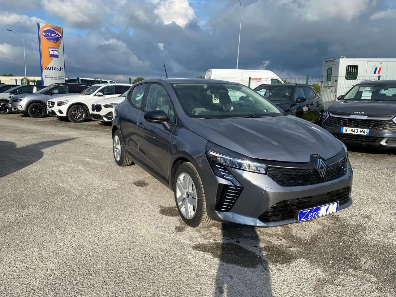 Renault Clio 2025 gris schiste vue 3/4 avant avec phares LED et calandre noire sur parking extérieur.