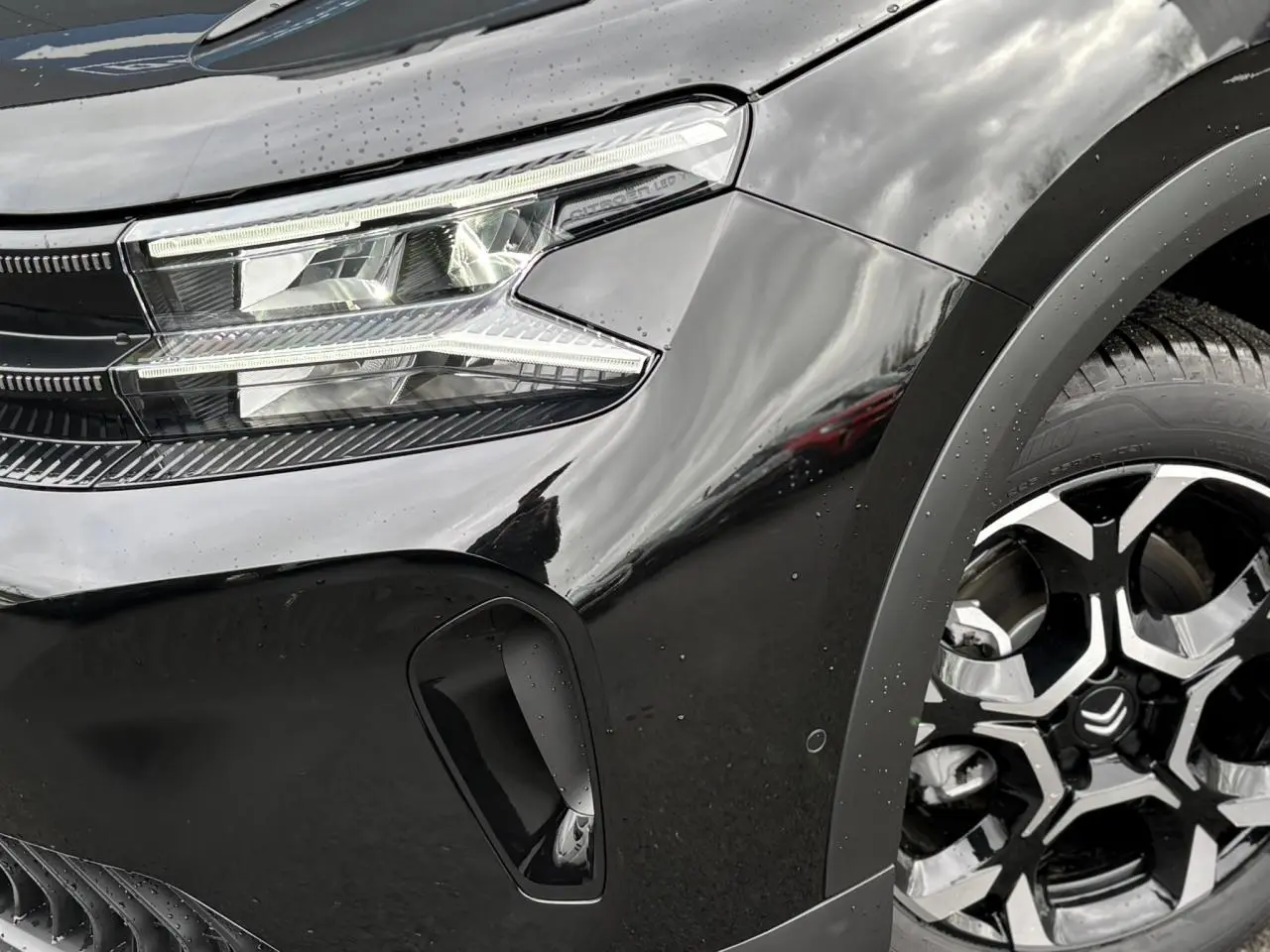 Gros plan sur l'avant droit noir Perla du Citroën C5 Aircross Hybrid, mettant en valeur le phare LED et la jante alliage bicolore.