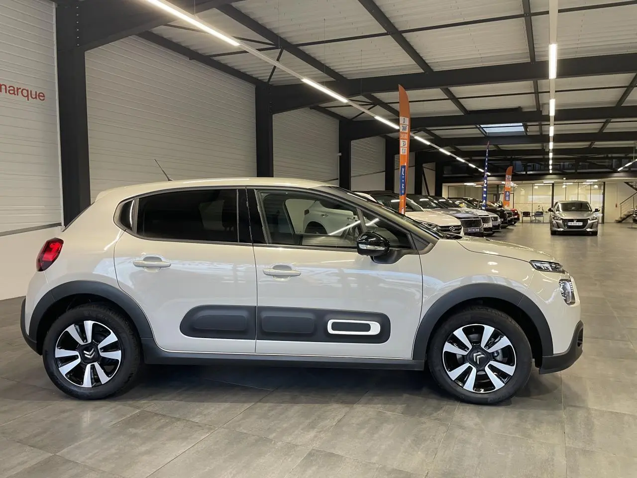 Vue latérale droite d'une Citroën C3 beige clair 2024 avec Airbump noirs et jantes alliage diamantées en intérieur showroom.