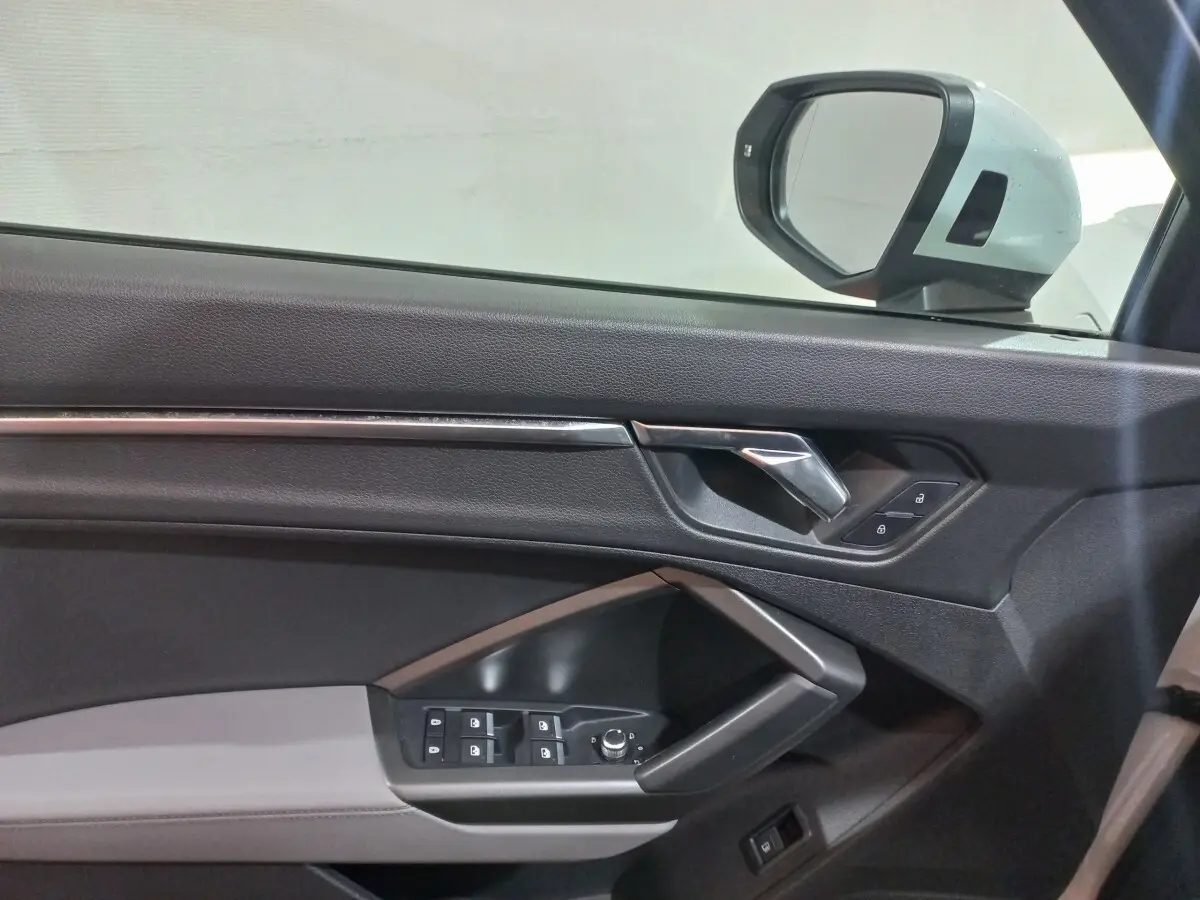 Vue intérieure côté gauche de la porte d’un Audi Q3 blanc, avec commandes de vitres et rétroviseur électrique.