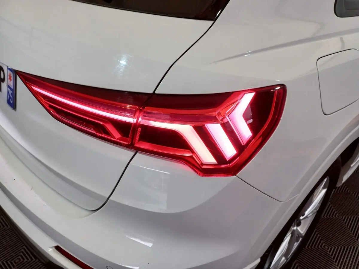 Feu arrière droit allumé d’un Audi Q3 blanc, vue rapprochée sur la partie arrière droite du véhicule.