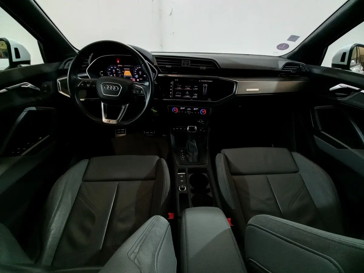 Vue intérieure avant de l'Audi Q3 blanc 45 TFSI E 245 S tronic S line, avec tableau de bord numérique et volant cuir multifonctions.