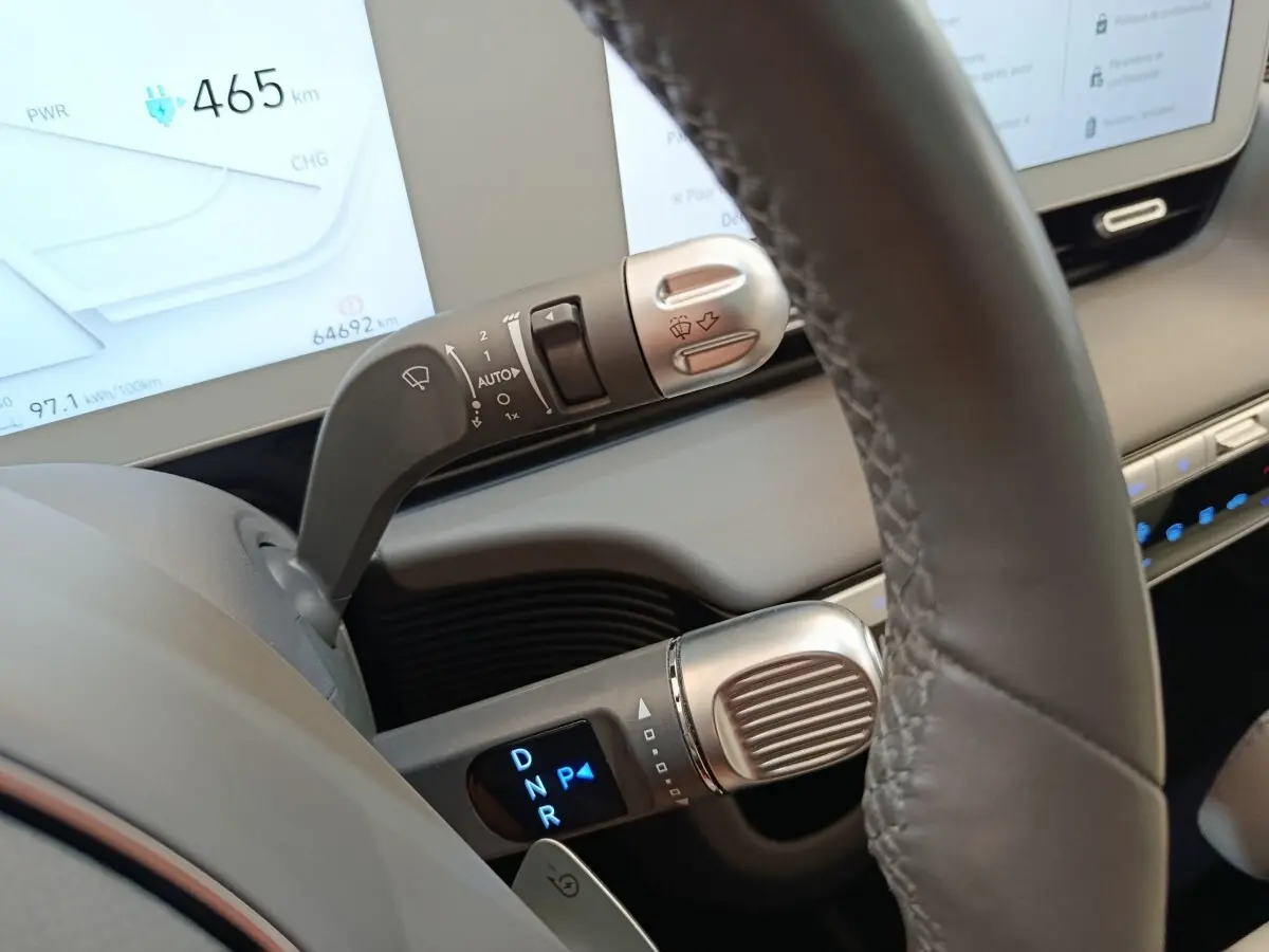 Gros plan sur le levier de vitesses et commandes au volant en cuir gris d’une Hyundai IONIQ BEV beige, tableau de bord numérique visible.