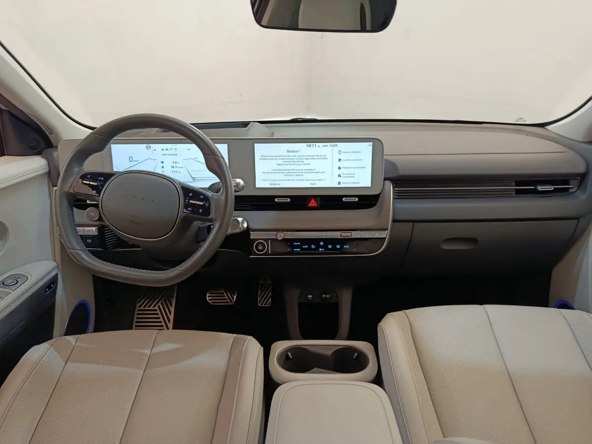Vue intérieure avant de la Hyundai IONIQ BEV beige 2023, tableau de bord moderne avec double écran tactile et volant cuir.