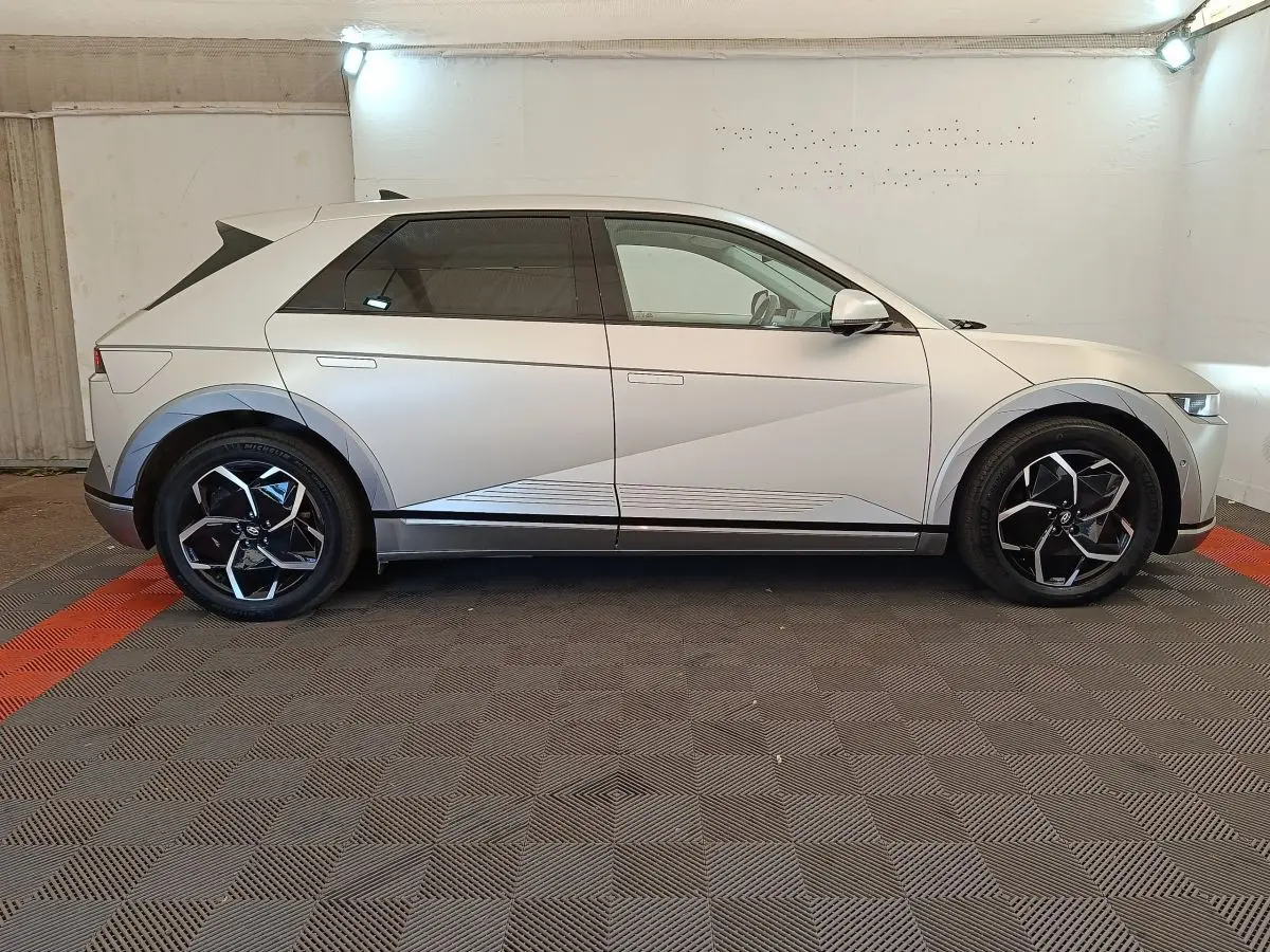 Vue de profil côté gauche d'une Hyundai IONIQ électrique beige 2023 avec jantes noires et détails géométriques sur la carrosserie.