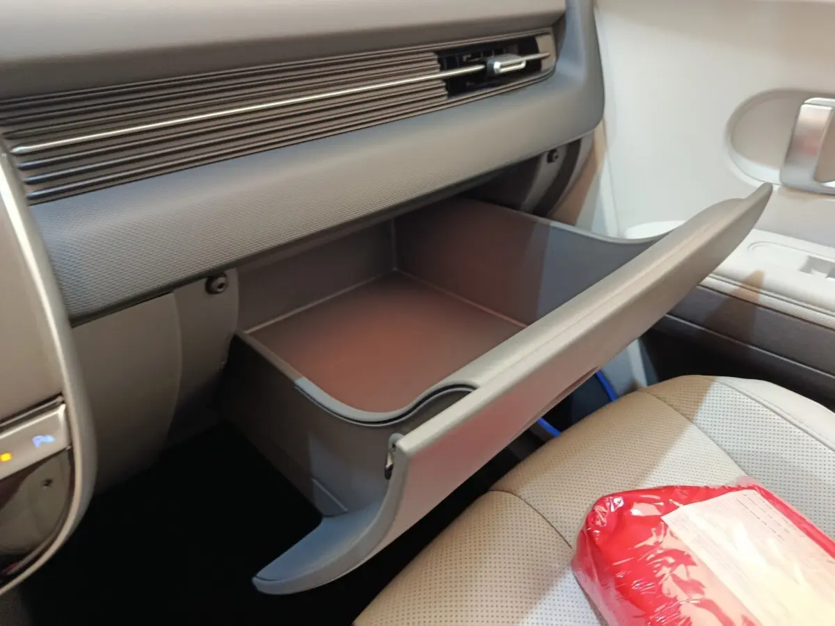 Intérieur de la Hyundai IONIQ BEV 77KWH AWD Executive 2023, vue de la boîte à gants ouverte côté passager beige.