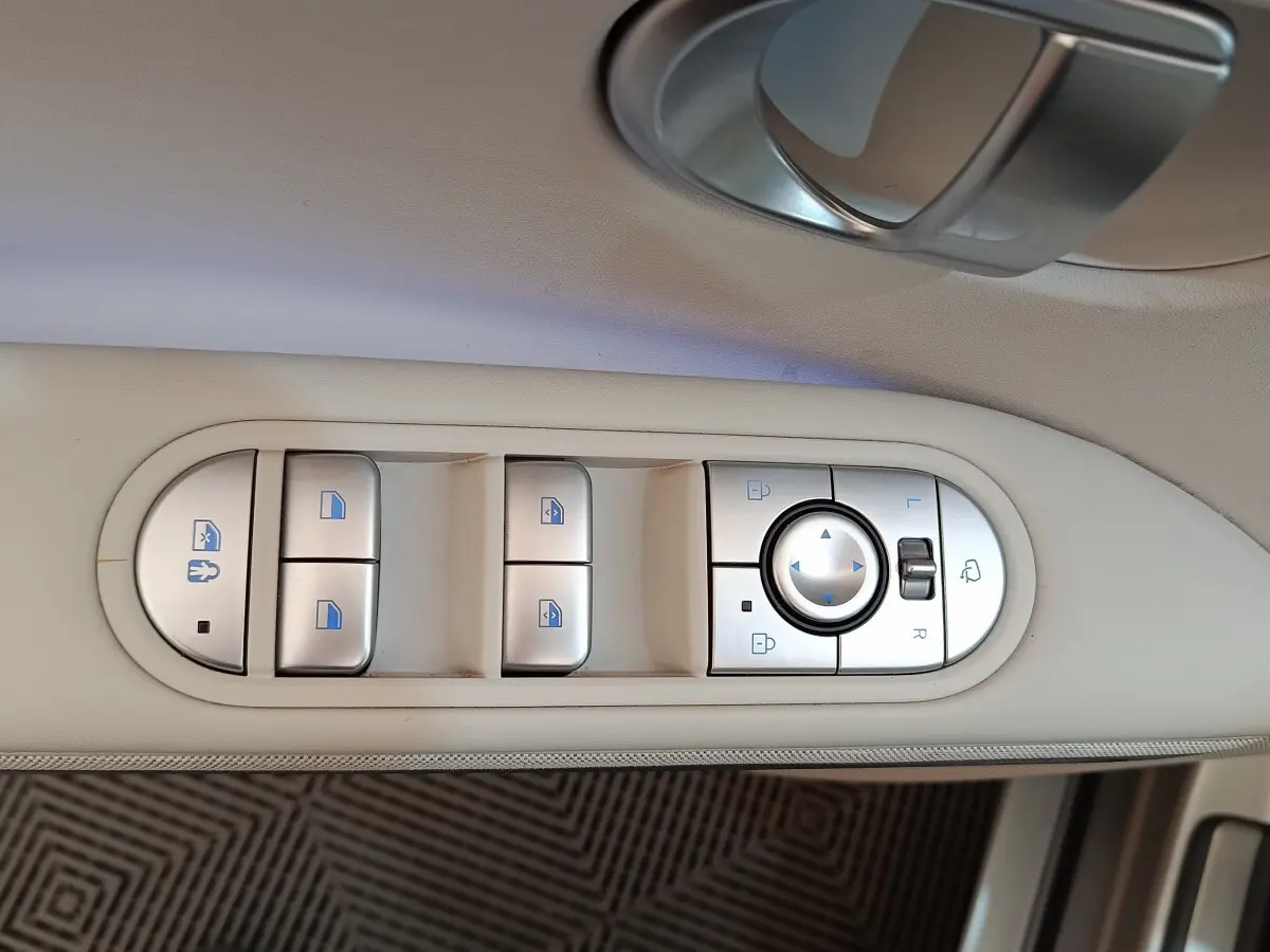 Gros plan sur les commandes de lève-vitres et rétroviseurs sur la porte beige intérieure d'une Hyundai IONIQ électrique 2023.