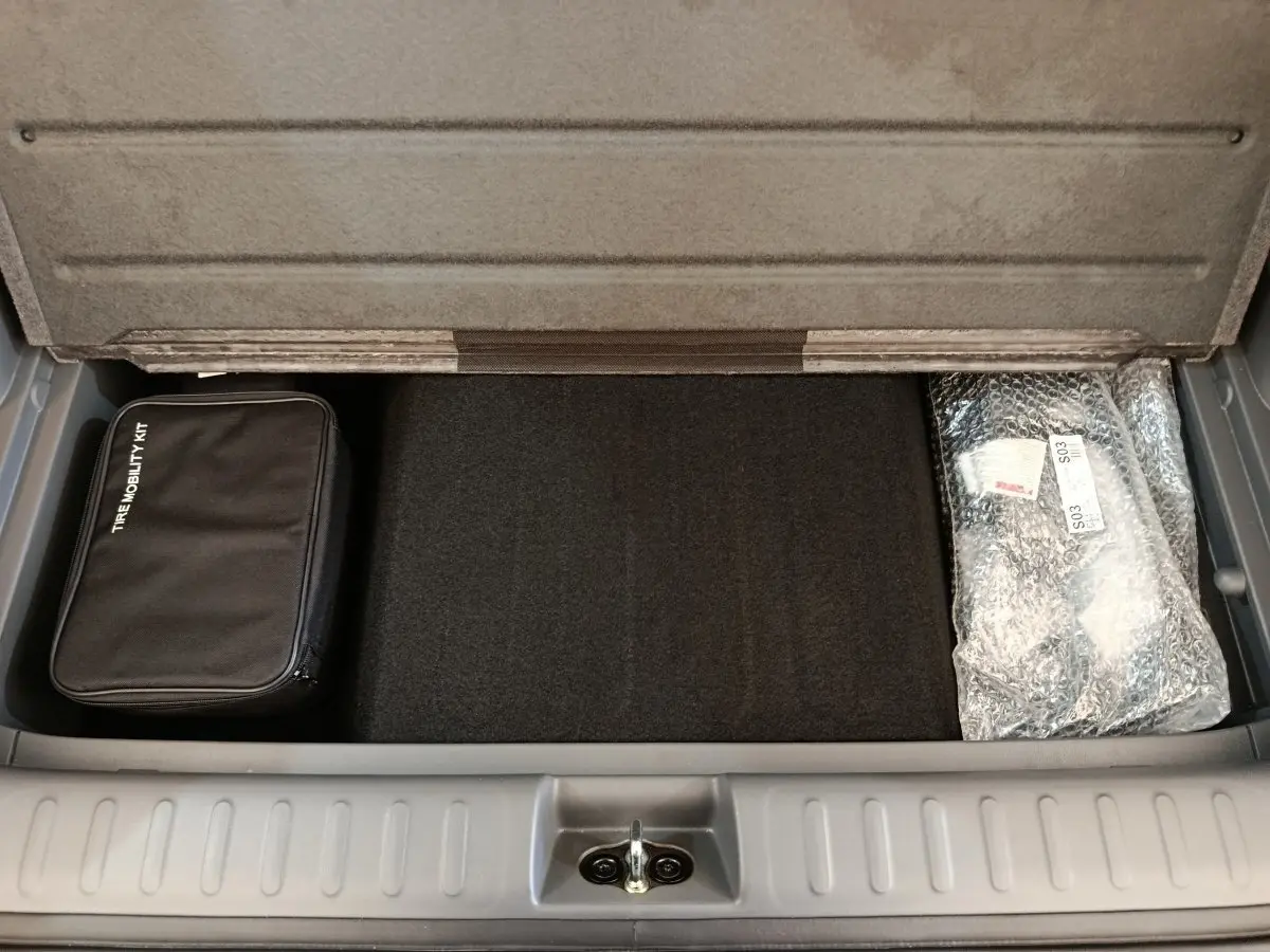 Coffre ouvert de Hyundai IONIQ beige 2023, vue plongeante sur espace de rangement avec kit de mobilité et accessoires emballés.