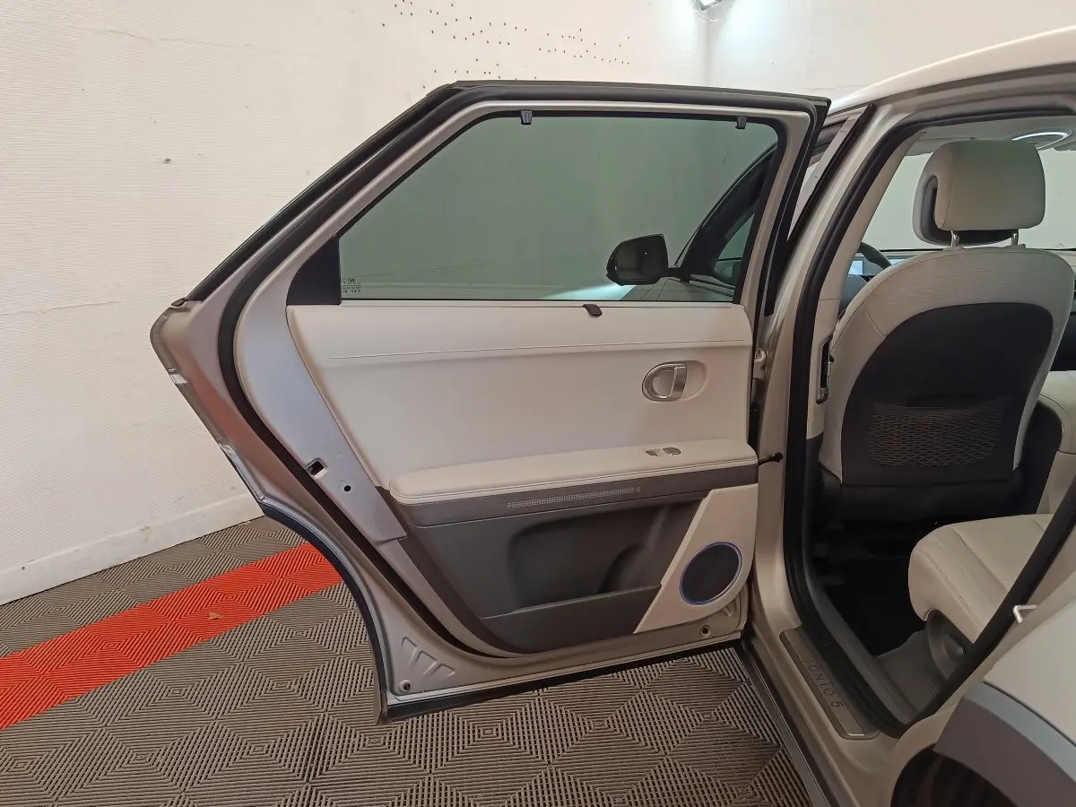 Vue intérieure côté gauche arrière d'une Hyundai IONIQ beige 2023, porte ouverte montrant la garniture claire et les sièges assortis.