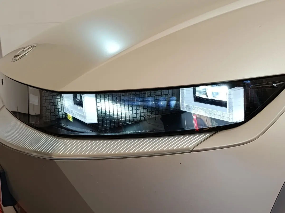 Gros plan sur le phare avant droit allumé d'une Hyundai IONIQ beige électrique, soulignant son design moderne.