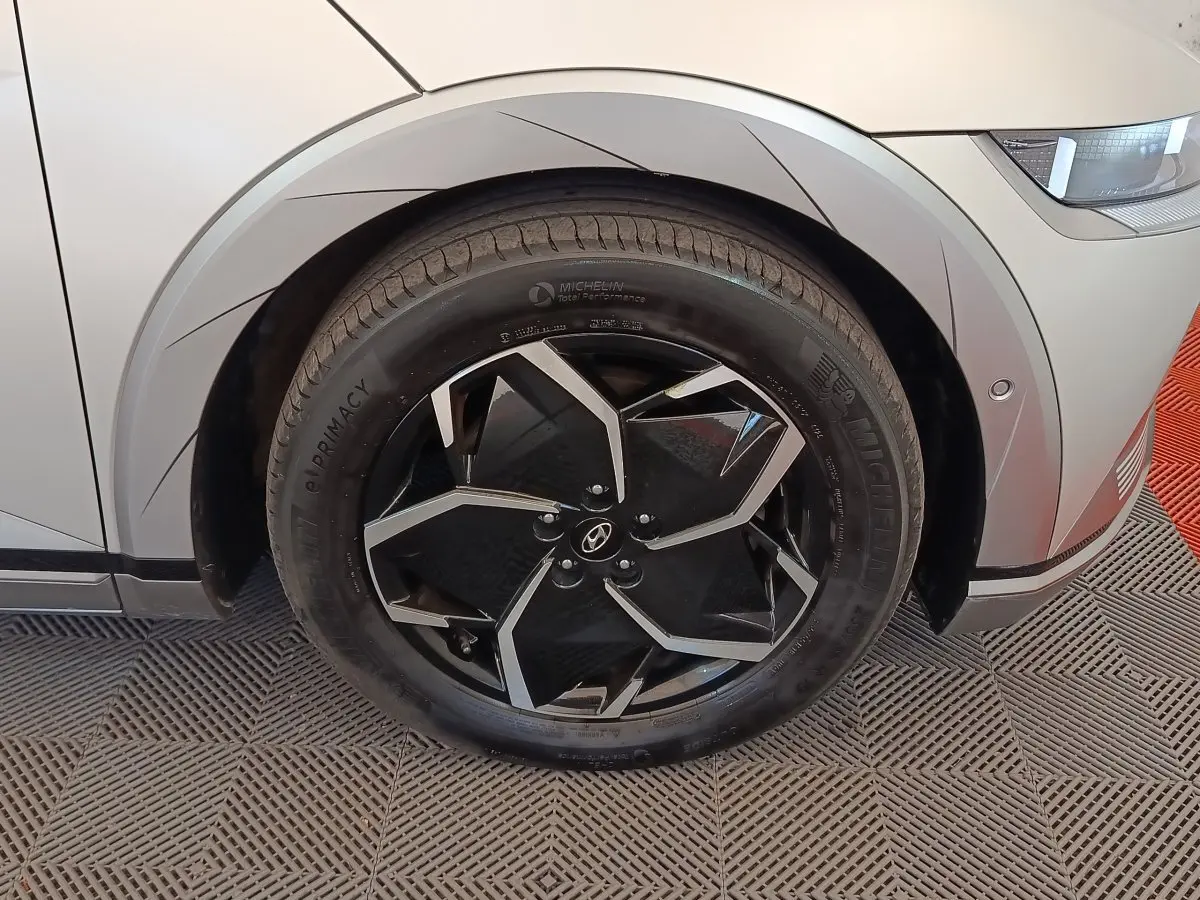 Gros plan sur la roue avant gauche noire et argentée d'une Hyundai IONIQ beige, avec partie avant droite visible.