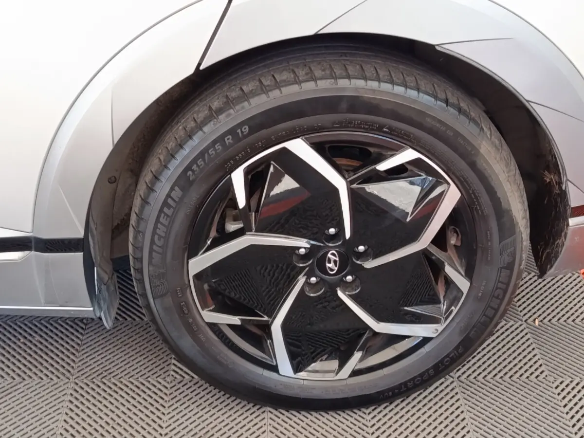 Gros plan sur la roue avant droite noire et argentée d'une Hyundai IONIQ beige, mettant en valeur la jante au design géométrique.