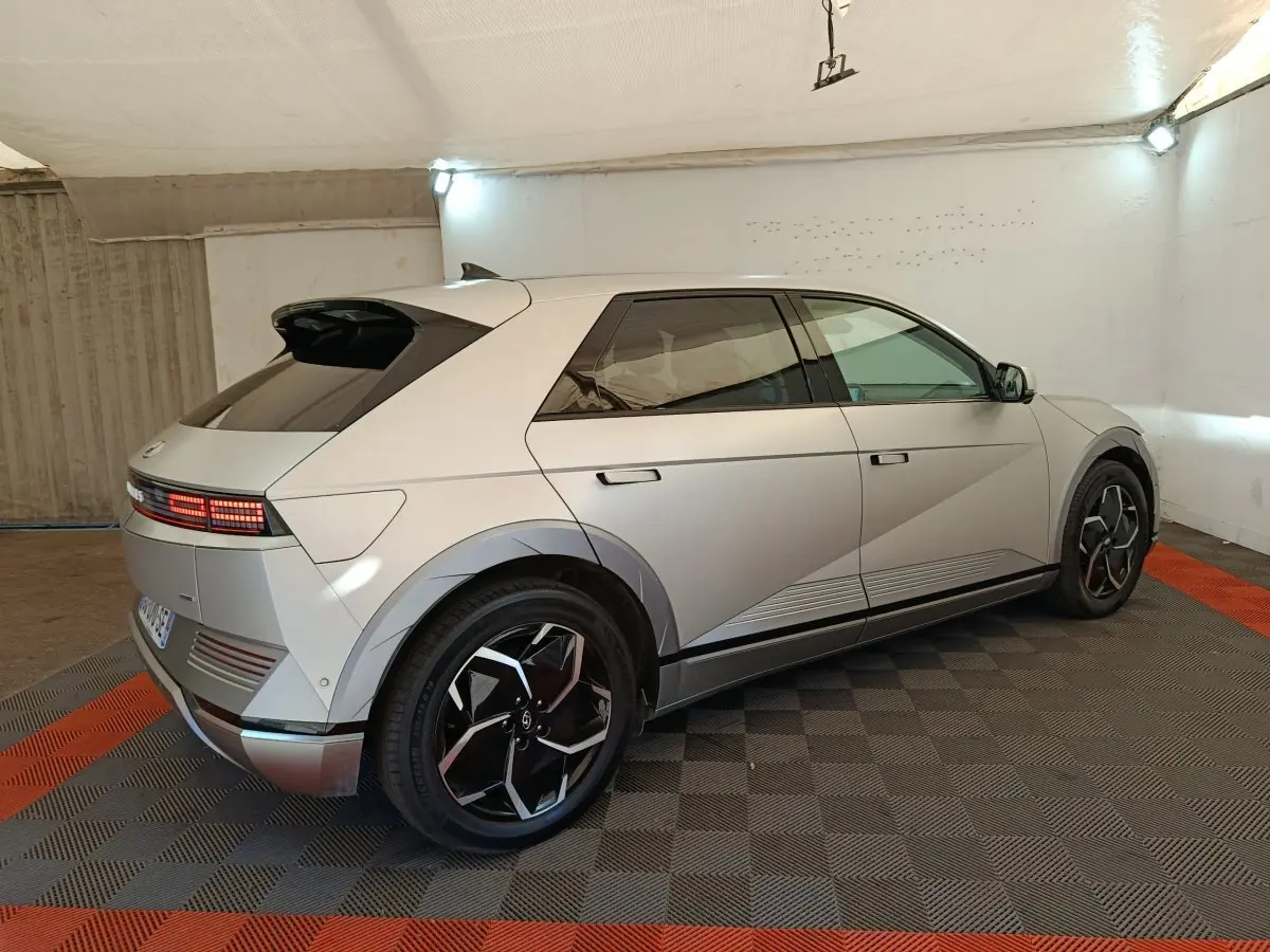 Vue 3/4 arrière droite d'une Hyundai IONIQ 5 beige électrique, avec feux arrière LED et jantes noires distinctives.
