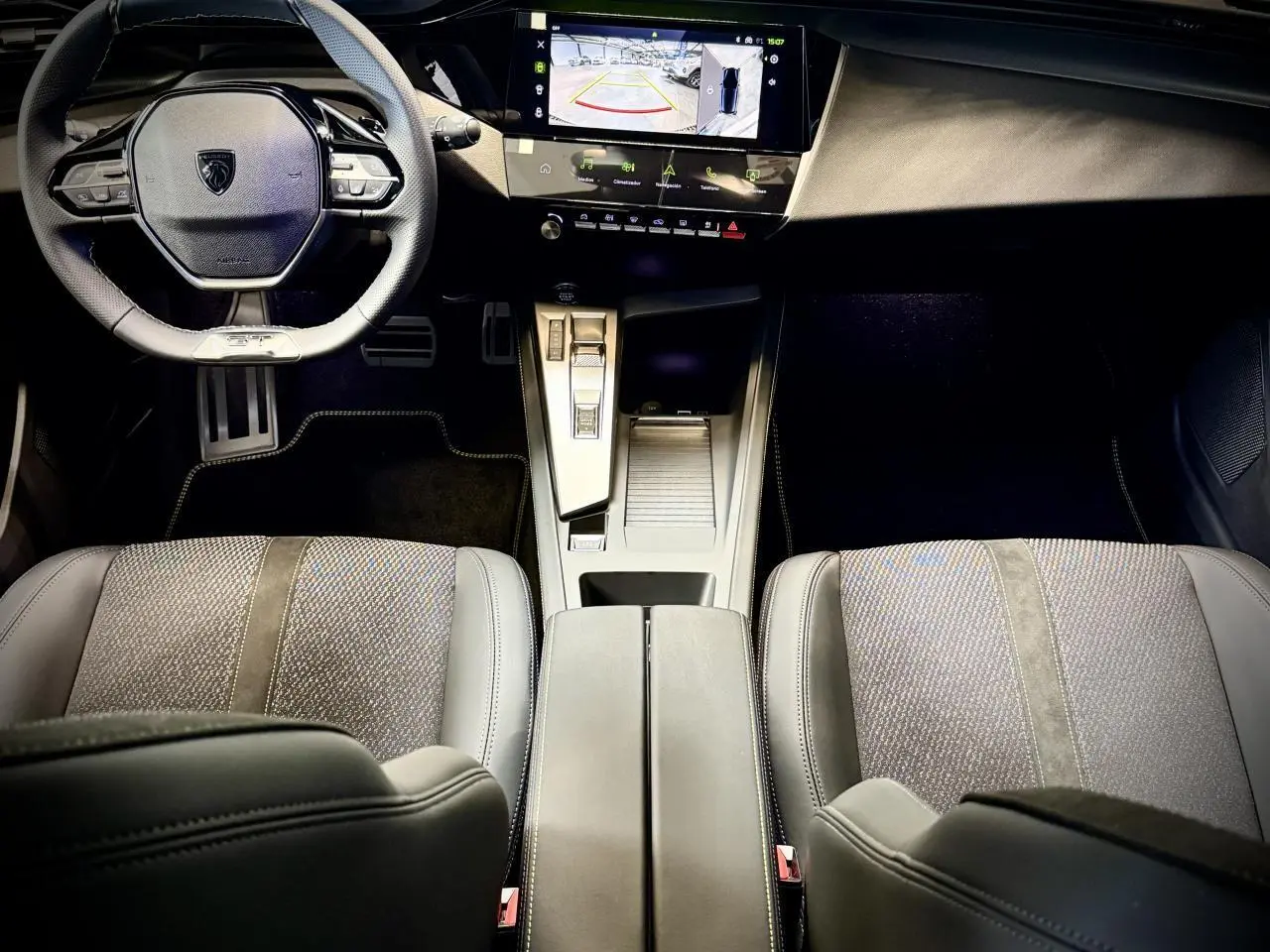 Vue intérieure avant de la Peugeot 308 GT 2025, montrant le volant cuir, la console centrale moderne et les sièges tissu/TEP gris.