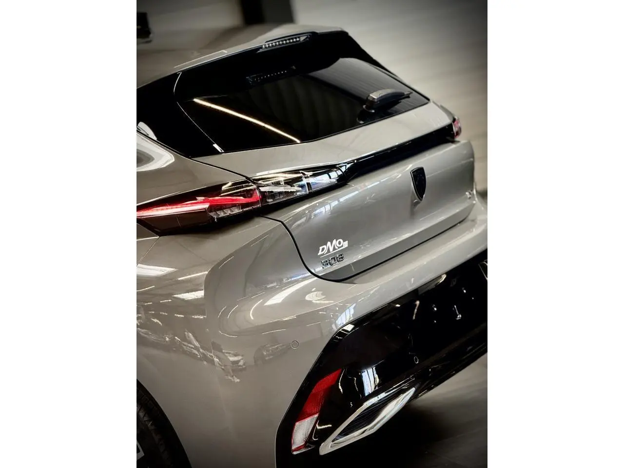 Vue 3/4 arrière droite d'une Peugeot 308 gris selenium avec feux arrière à signature lumineuse griffe à griffe.