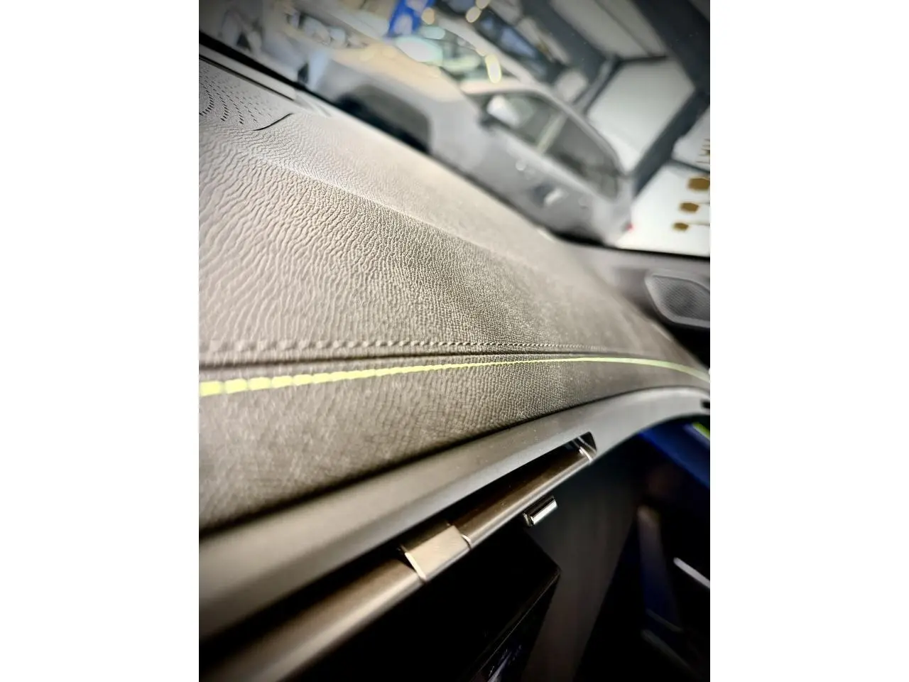 Gros plan sur la planche de bord texturée avec surpiqûres vertes de la Peugeot 308 GT 2025 gris selenium.