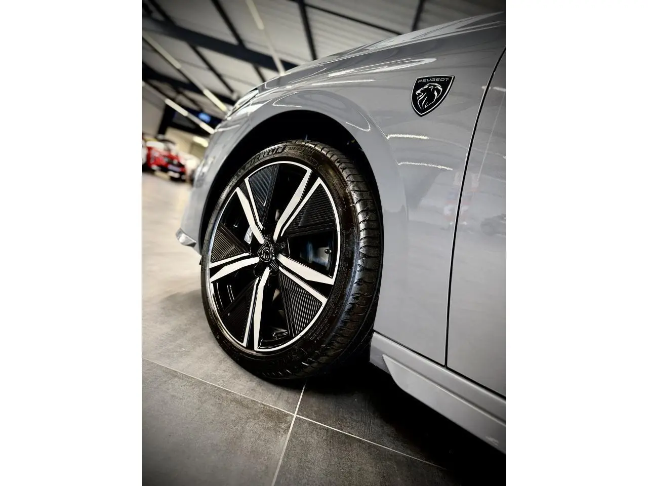 Gros plan sur la roue avant gauche et l'aile gris sélénium d'une Peugeot 308 GT avec logo lion noir brillant.