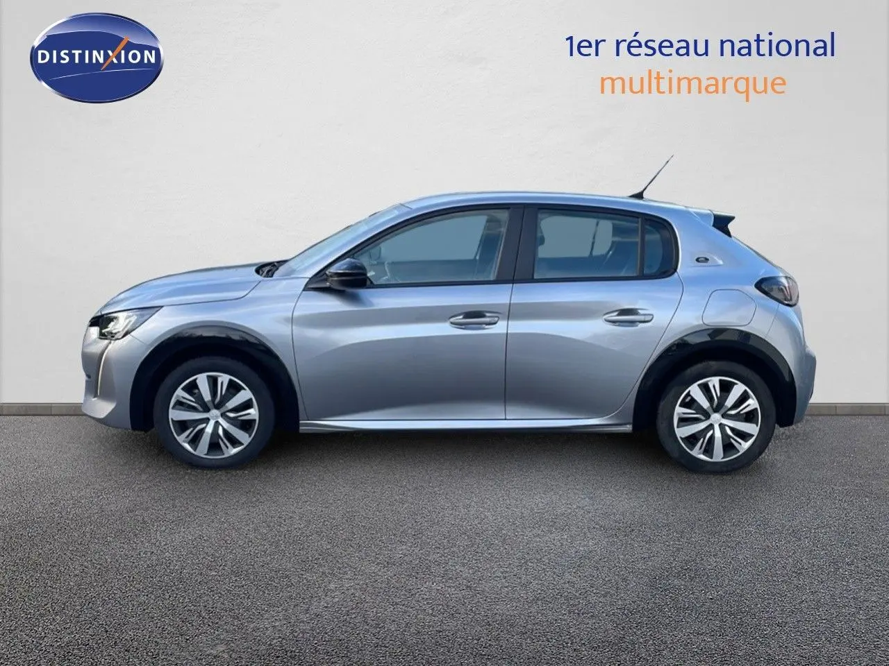 Profil côté gauche d'une Peugeot 208 électrique gris artense, version Active Business, garée devant un mur blanc.