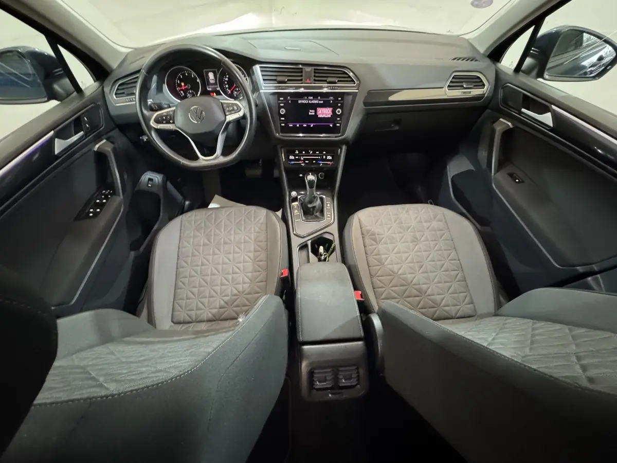 Vue intérieure avant du Volkswagen Tiguan 1.5 TSI 2021, montrant tableau de bord, volant multifonctions et sièges gris à motifs.