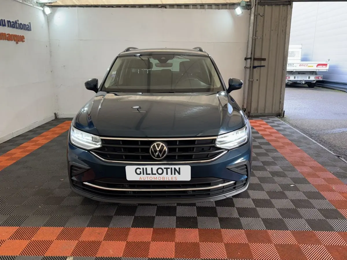 Vue frontale d'un Volkswagen Tiguan bleu avec phares LED allumés et rails de toit noirs en intérieur.