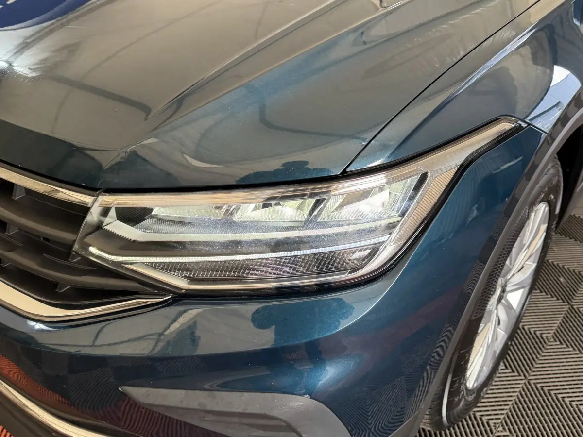 Gros plan sur l'avant droit bleu métallisé du Volkswagen Tiguan 2021, mettant en valeur le phare LED et la calandre.